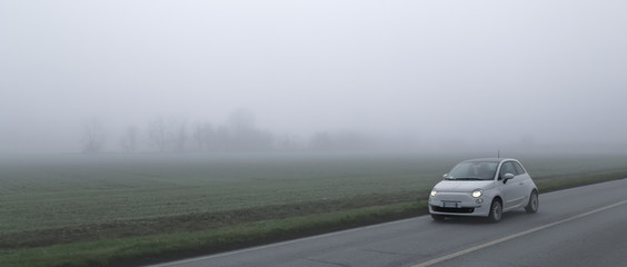Small car runs along a country road on a foggy day