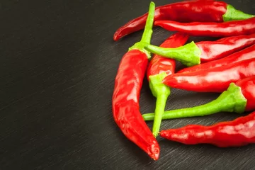 Glasschilderij  Red chilly pepper on wooden black background. Red hot chili peppers.  Domestic cultivation extra hot chilli burn. Growing chili peppers. Spicy seasoning food. Healthy spices.    © martinfredy