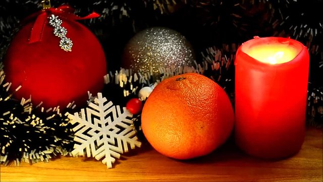 Cristmas toy, tangerine and burning candle  on background of pine-needles