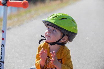 Fototapeta na wymiar Happy child in green helmet with kick scooter like sport.