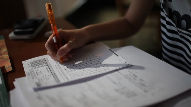 The Girl hand is filling a blank on answer paper with pencil