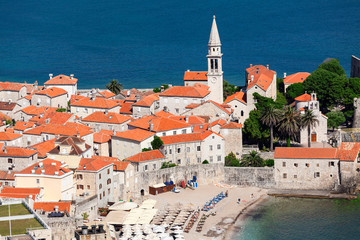 Fototapeta premium Bell tower of the Old Town of Budva city and Ricardova Glava beach. Aerial view with houses roofs. Adriatic sea. Montenegro