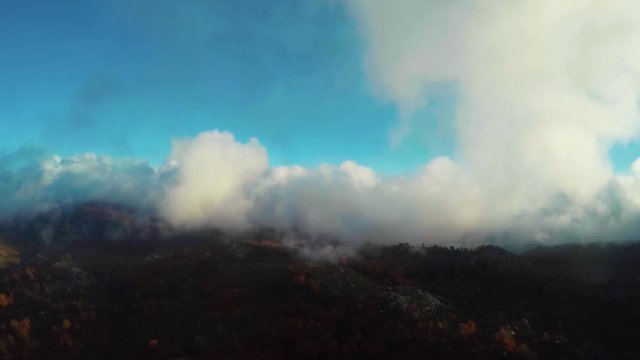 Aerial bird-eye view flight past cloud and then flying into larger cloud bright blue sky background and mountain landscape below beautiful scene quadcopter stable forward bird view flight relaxing 4k