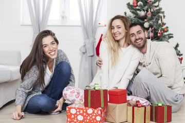 Obraz na płótnie Canvas Friends sitting next to Christmas tree with presents