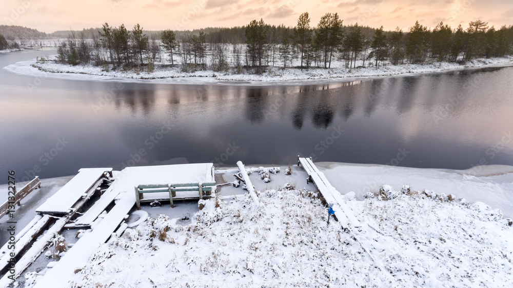 Sticker Snow covered timber pier on wintry river with open water. Winter river bend is in swamp. Karelia, Russia