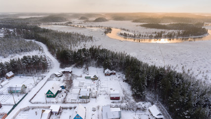 Small Russian village with timber houses is in evergreen forest and swamp at cold winter evening time. Aerial view in sunset light. Karelia, Russia