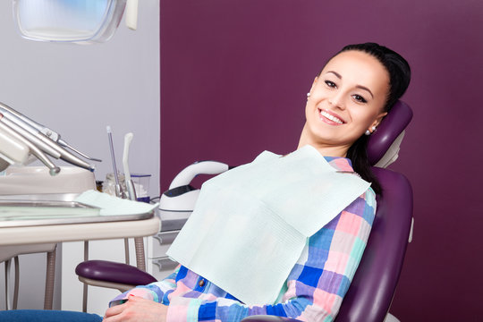 Young Woman Patient In Checkered Shirt With Perfect Straight White Teeth Waiting For Dentist In Dental Chair And Smiling Relaxed, Ready For A Check-up. Beautiful Woman Smile