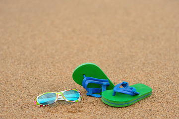 Fototapeta na wymiar A pair of green and blue flip flops with colorful sunglasses