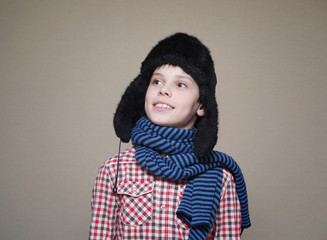 Boy in a scarf and cap with ear-flaps on grey background. 