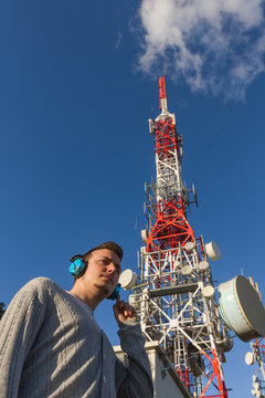 Hombre Joven  con Cascos al lado de una Antena de Telecomunicaciones