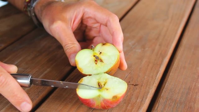 A man cuts the worm-eaten apple on a wooden table