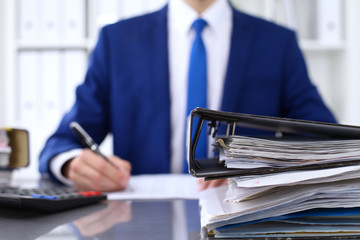 Binders with papers are waiting to be processed with businessman back in blur. Accounting planning budget, audit, insurance  and business concept