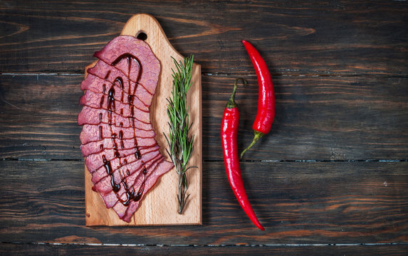 Sliced ham, chilli pepper, rosemary on a wooden board