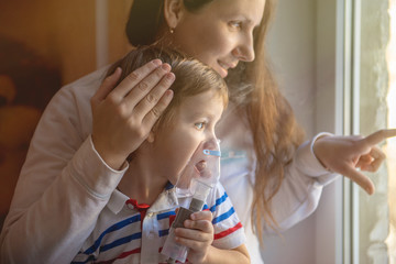 Young woman with son doing inhalation with a nebulizer at home - obrazy, fototapety, plakaty