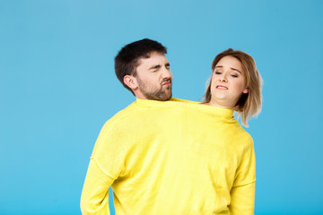 Displeased young couple in yellow sweater posing over blue background.