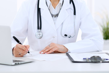 Female doctor at the table and filling up medical form. Medicine and health care concept.