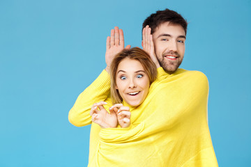 Young beautiful couple in one yellow sweater posing smiling having fun over blue background.
