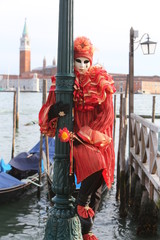 Venice Carnival masked man sitting on a pole in front of gondola