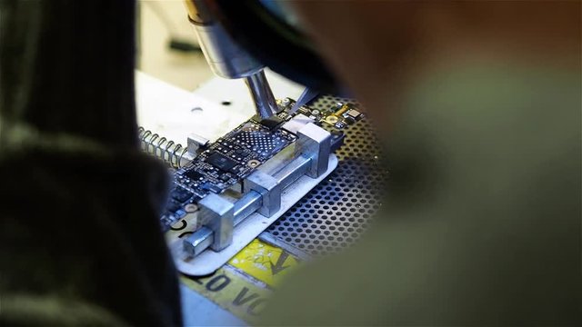 White man mounts new chip to motherboard of smartphone iphone in workshop