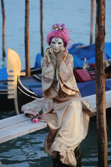 Venice Carnival - young lady with golden and pink mask on the pier with gondolas