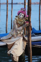 Obraz premium Venice Carnival - young lady with golden and pink mask on the pier with gondolas