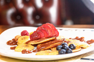 Sliced strawberries lying on the pancakes with chocolate sauce.
