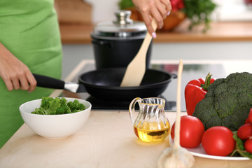 Fresh vegetables, salad and vegetable oil at the background of  woman is cooking by the stove in the kitchen