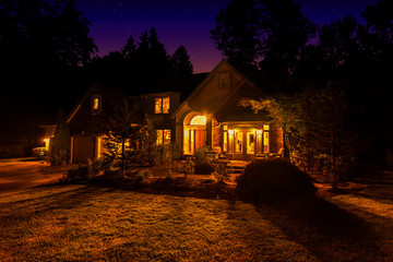 Suburban home at night with windows lit up and light spilling out onto the front lawn