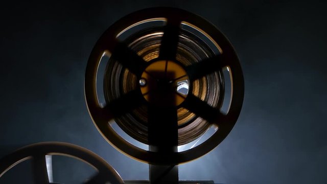 Reels twisting film on the projector in motion. Side view
