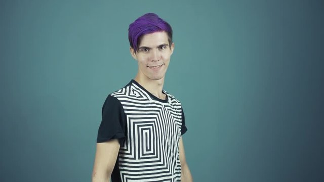 Young blogger with purple hair looking at camera and smiling in web studio gray background