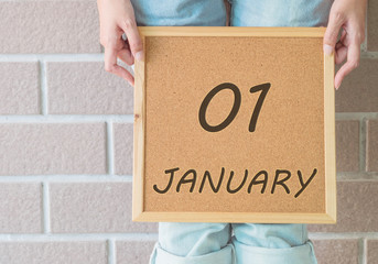 Closeup calendar at the cork board in hand of asian woman in front of her legs with 1 january word on brick wall textured background