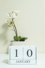 Closeup white wooden calendar with black 10 january word with white orchid flower on white wood desk and cream color wallpaper in room textured background , selective focus at the calendar