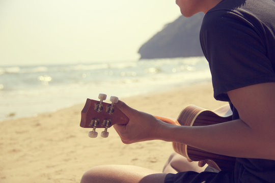 A man playing ukulele on the sandy beach in close up view. trave