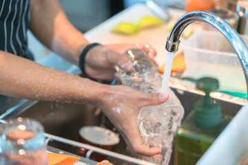 Human hand washing dish or pouring glass with fresh drink water at kitchen faucet
