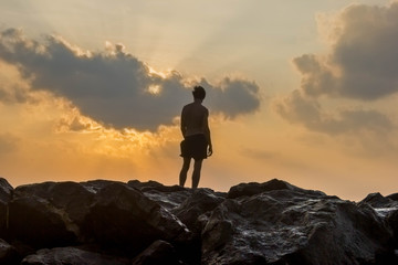 person standing on rocks seaside sunset silhouette frontback lig