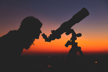 Fototapeta na wymiar Girl looking at the stars with telescope beside her and de-focused city lights. 