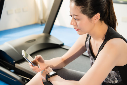 Asian Woman Rest On Treadmill Use Smartphone And Smartwatch