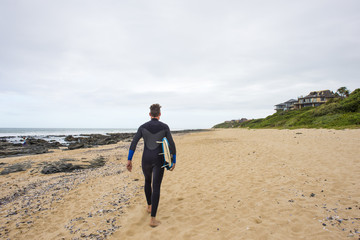 Surfer walks along beach with surfboard