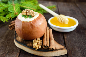 Baked apple stuffed with cottage cheese, cinnamon, walnuts with honey and mint on a dark wooden background. Close-up.