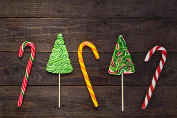 Christmas sweets: bright colored candies in the form of a cane and fir tree on a dark wooden background. Celebratory background.