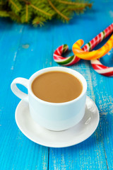 Christmas theme. A cup of coffee with milk (cappuccino), in the form of bright candy canes and green spruce branches on a blue background.