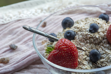 Glass bowl with old teaspoon, cereals, strawberries and blueberries on the pink tissue