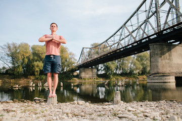 yoga man standing near the river on the stump