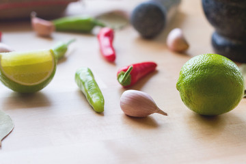 A selective focus of green lemon on wooden table, an Asian style preparation food for cooking,pestle and mortar, garlic cloves, brown bag of herb, red and green chillies, knife lying on table