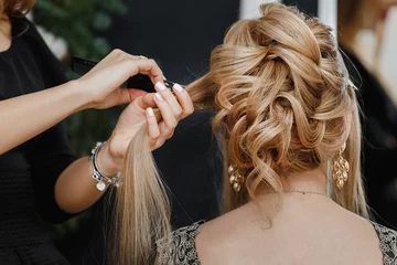 Rolgordijnen Kapsalon Hairdresser makes upper bun wedding hairstyle close-up on sandy blond hair of beautiful woman