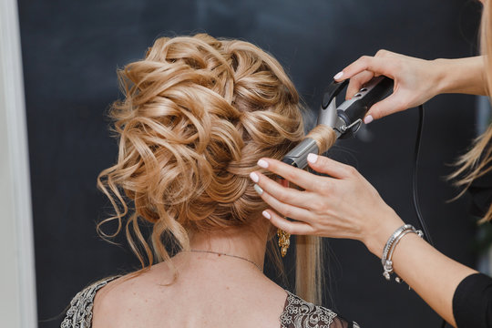 Hairdresser makes a woman sandy hair high fashion wedding or evening hairstyle