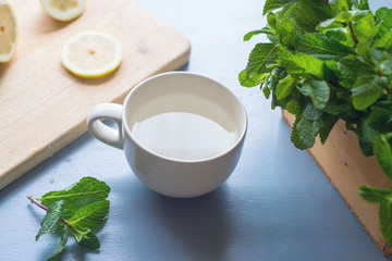 An ingredients for peppermint tea on light blue rustic table, lemon slices on chopping board,fresh mints in wooden box with peppermint leaves laying on table, healthy drink for winter,release stress