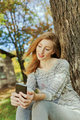 Beautiful girl with long blond hair and blue eyes looks on the phone. Location of autumn park.