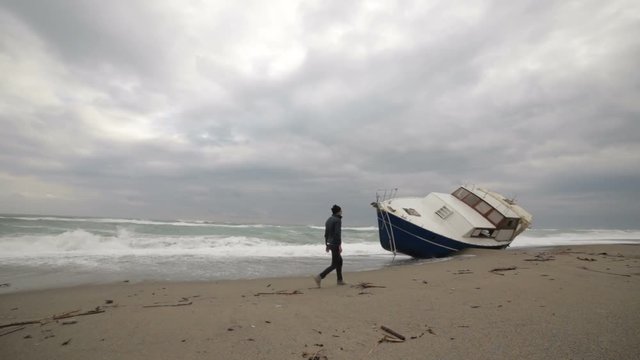 Uomo sta camminando sulla spiaggia di fianco a una barca arenata