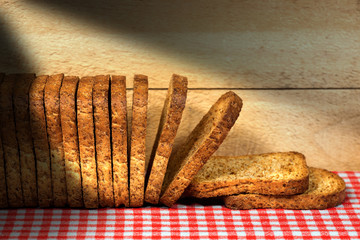 Healthy rusks of wholemeal flour on a table with checkered tablecloth and wooden wall